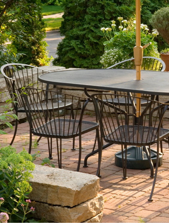 Terras met zwarte, metalen tafel en vier stoelen in een tuintje 