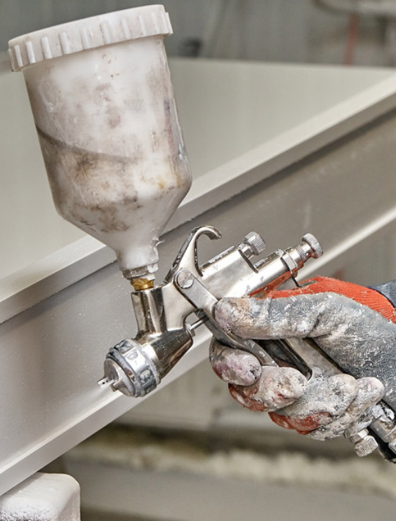 Hand met daarin een spuitpistool en de intentie om een stuk PVC te lakken